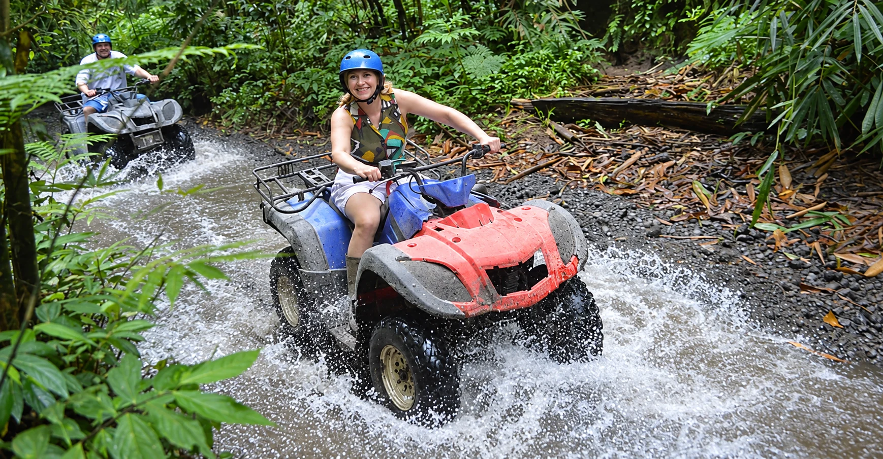 ATV riders crossing a stream on a forest trail in Bali.