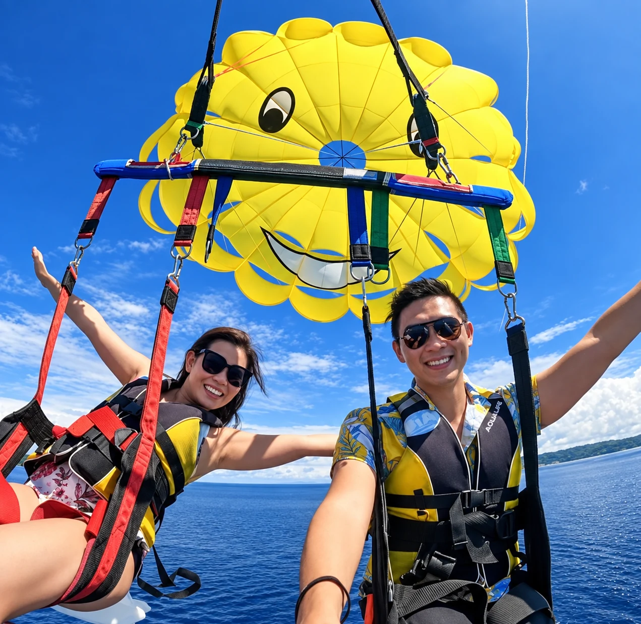 Two guests in parasailing harnesses beneath a yellow parachute.